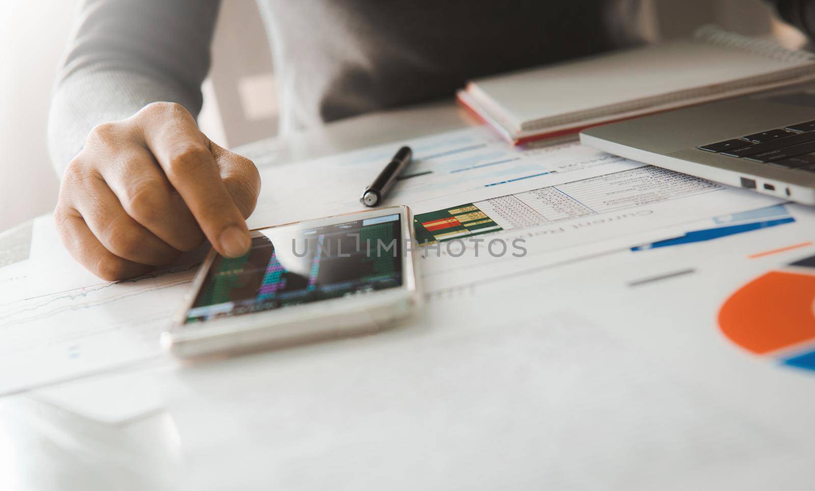 Businesswoman analyze business report graph and finance chart using smartphone and computer laptop at corporate office.