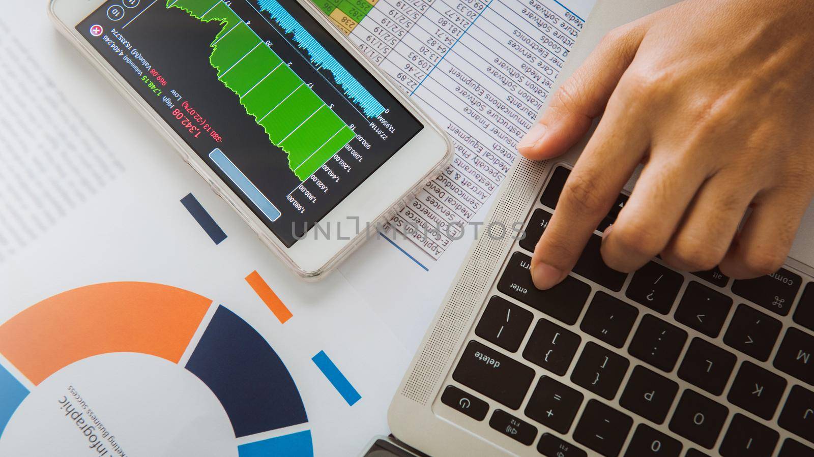 Businesswoman analyze business report graph and finance chart using smartphone and computer laptop at corporate office.