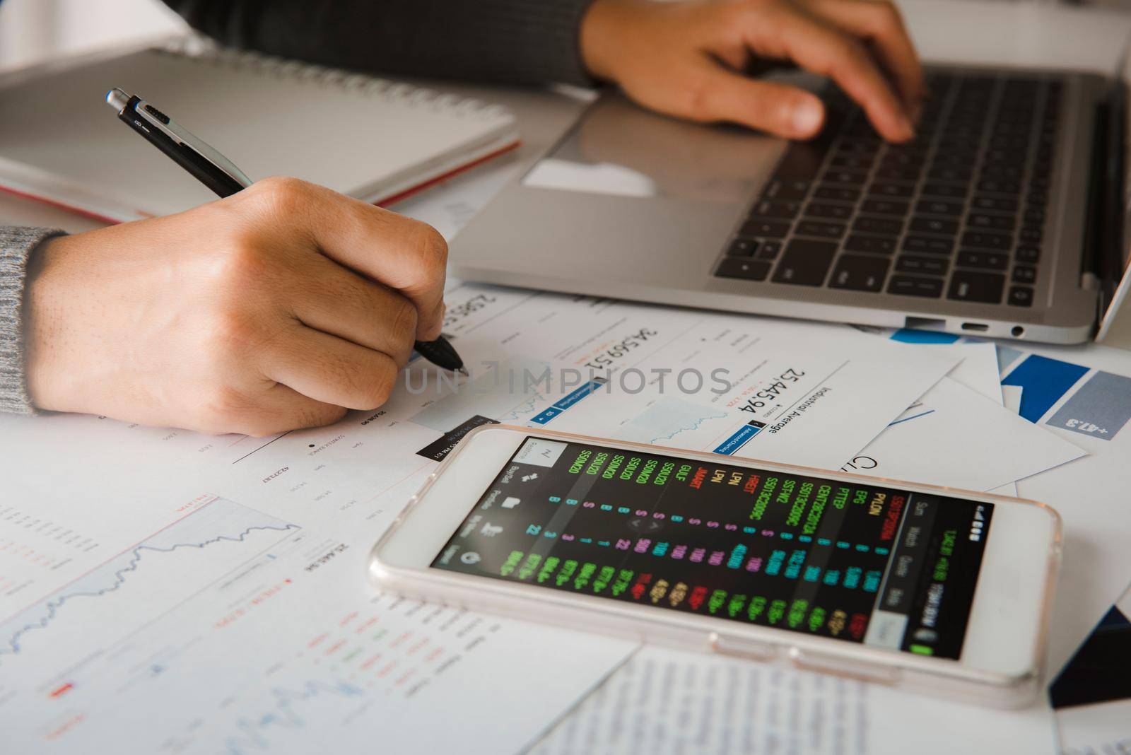 Businesswoman analyze business report graph and finance chart using smartphone and computer laptop at corporate office.