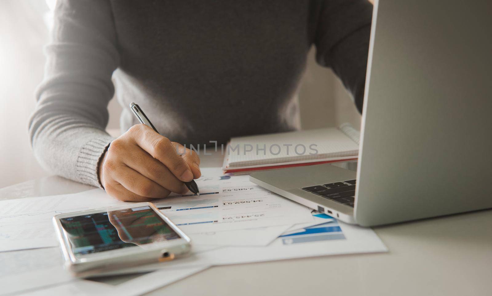 Business documents on table with smart phone and laptop computer and woman working in the background, Concept of finance economy, banking business and stock market research. by thanumporn