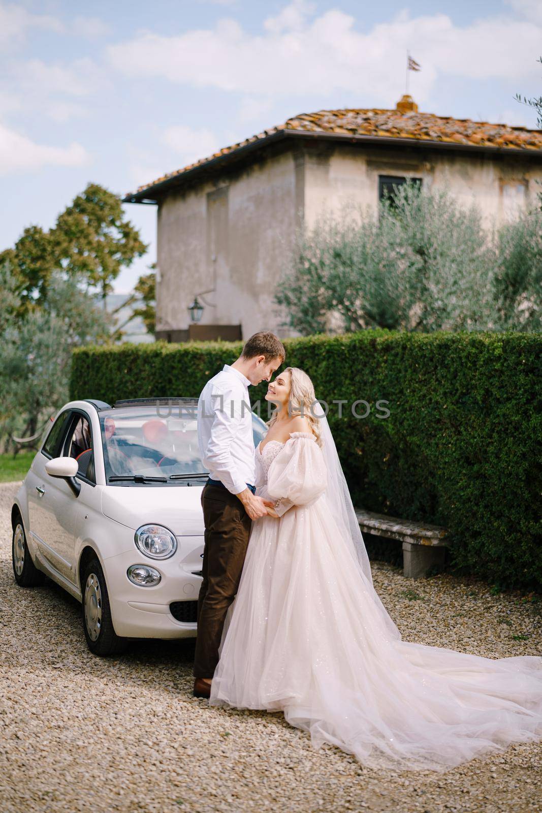Beautiful bride and groom looking at each other and holding hands in front of a convertible at the Villa in Tuscany