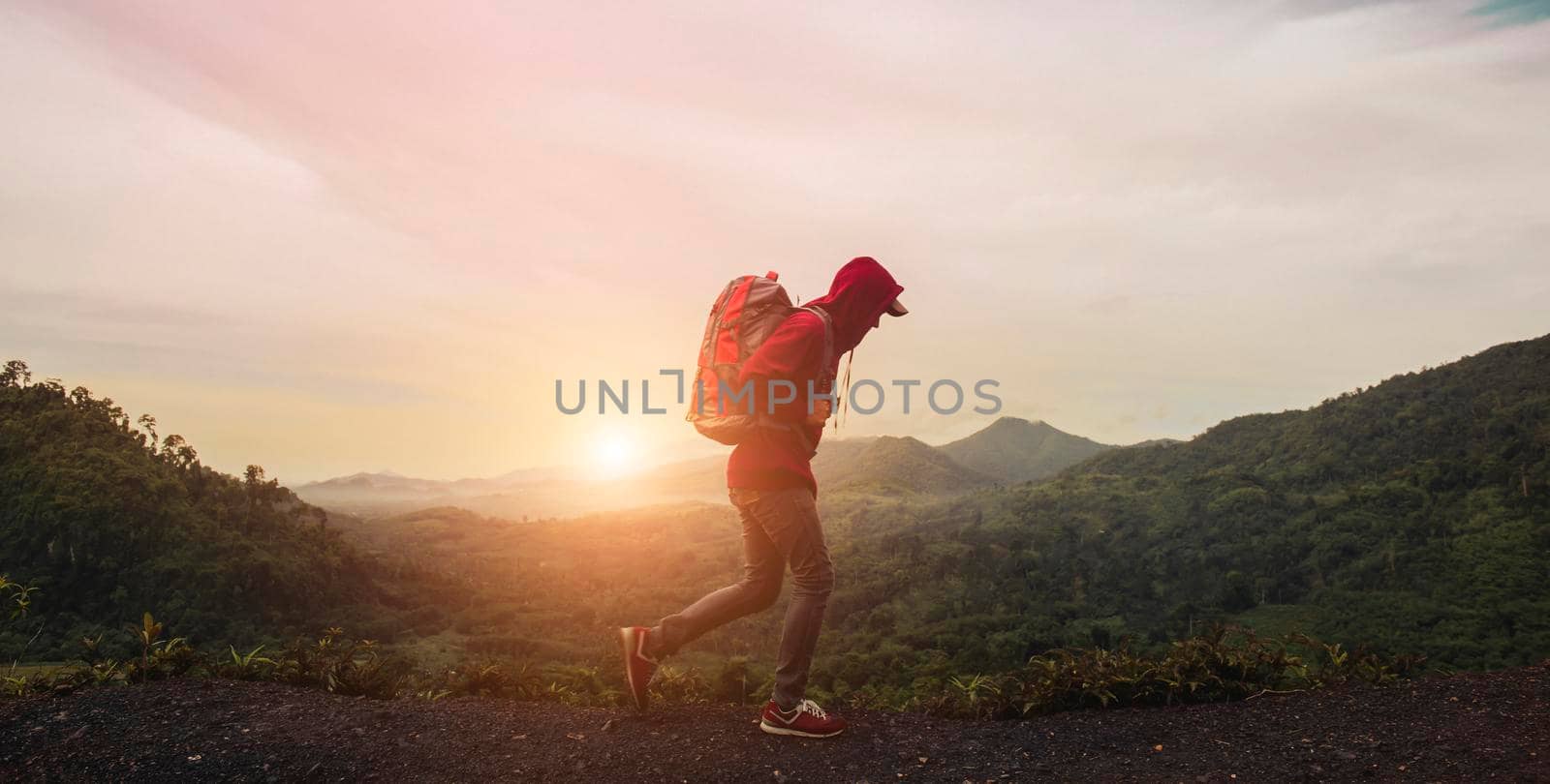 Young man with backpack  walking on path and heading to foggy mountain and sunrise in the morning. Tourist traveler on background valley landscape view. Concept of hiking, climbing and backpacking.