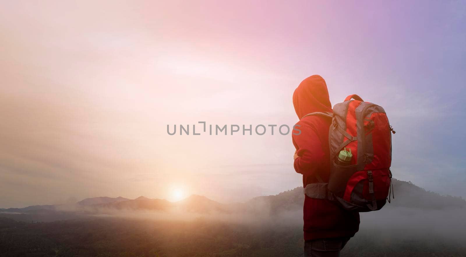 Back view of man traveler with backpack walking on path and heading to foggy mountain and sunrise in the morning. Concept of hiking, climbing and backpacking. by thanumporn