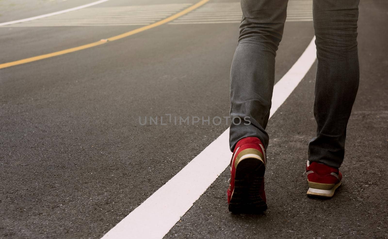 Close up view on man's legs in jeans and red sport shoe with sunlight   background.Travel Concept.