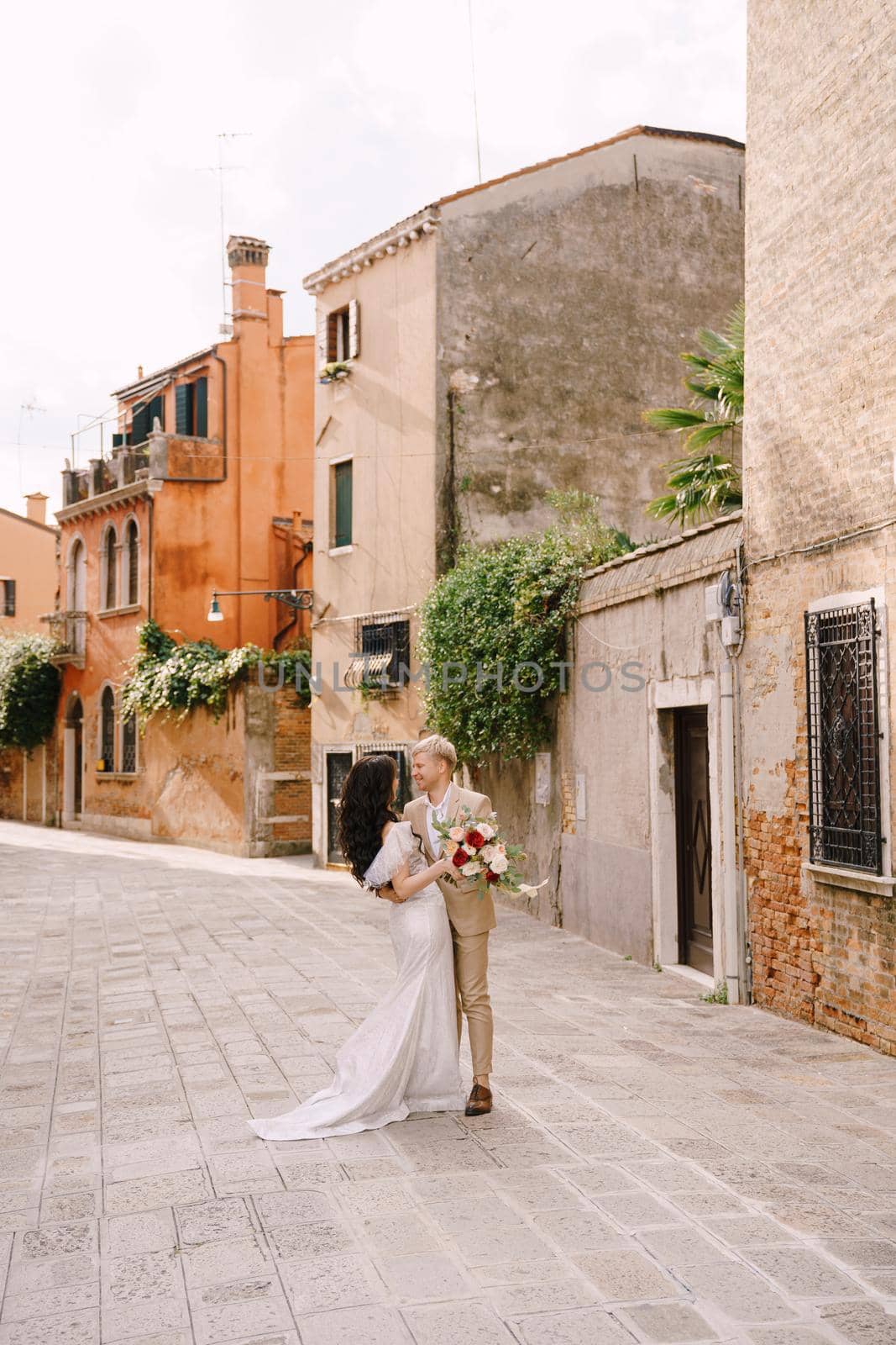 The bride and groom walk through the deserted streets of the city. Newlyweds hug, dance, hold hands against the backdrop of picturesque red brick houses.