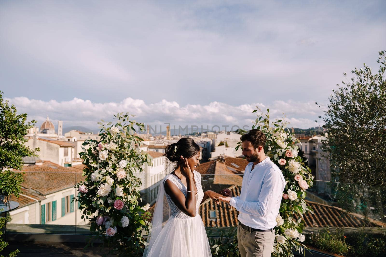 Destination fine-art wedding in Florence, Italy. Multiracial wedding couple. A wedding ceremony on the roof of the building, with cityscape views of the city and the Cathedral of Santa Maria Del Fiore by Nadtochiy