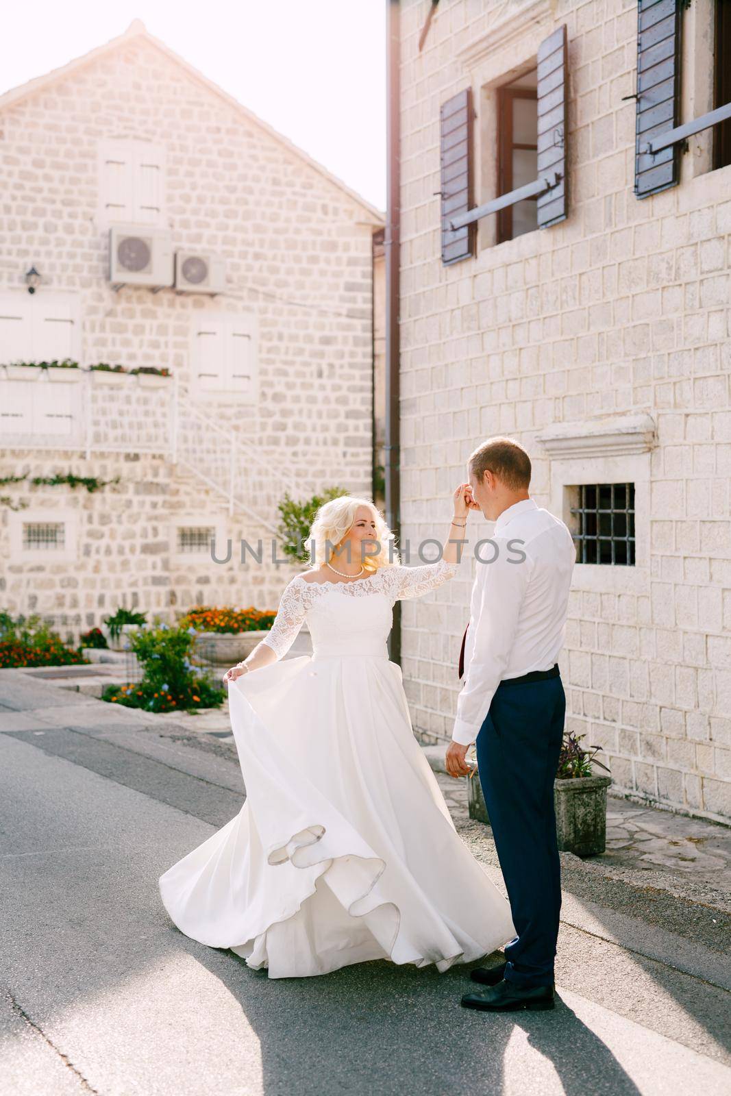 The bride and groom are dancing on the road near the beautiful white house in the old town of Perast by Nadtochiy