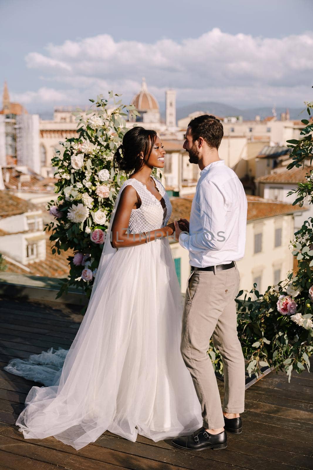 Interracial wedding couple. Destination fine-art wedding in Florence, Italy. A wedding ceremony on the roof of the building, with cityscape views of the city and Cathedral of Santa Maria Del Fiore