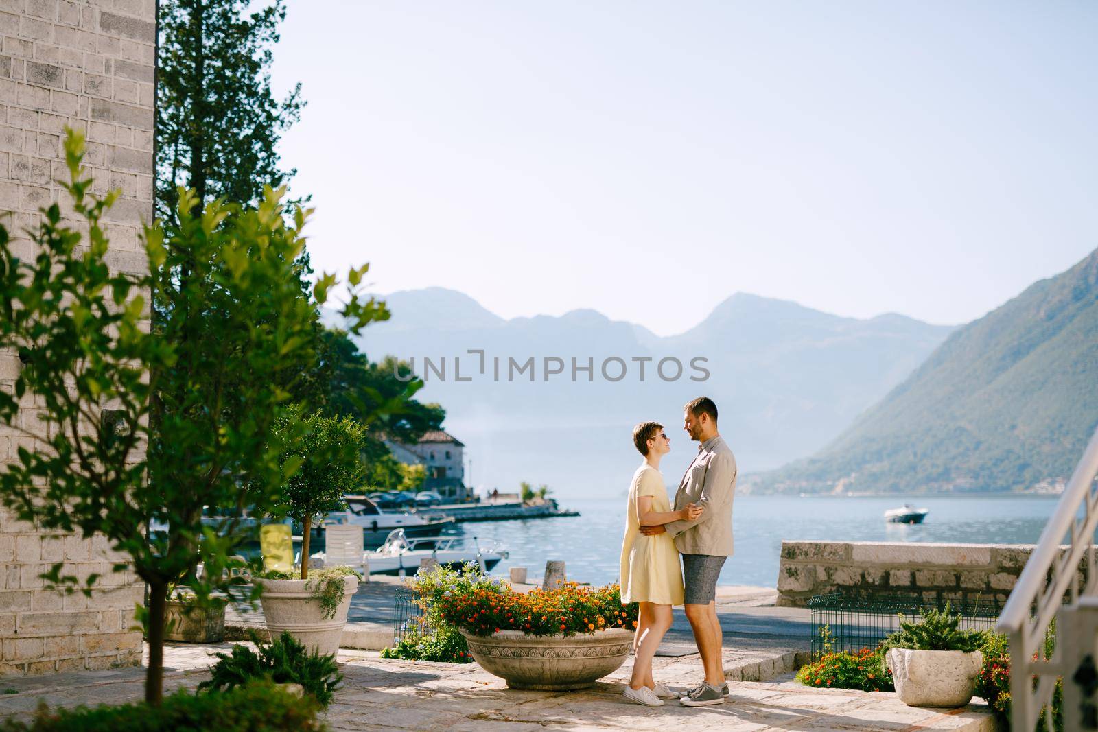 A man and a woman stand hugging in Perast on the shore of the Bay of Kotor and look at each other by Nadtochiy