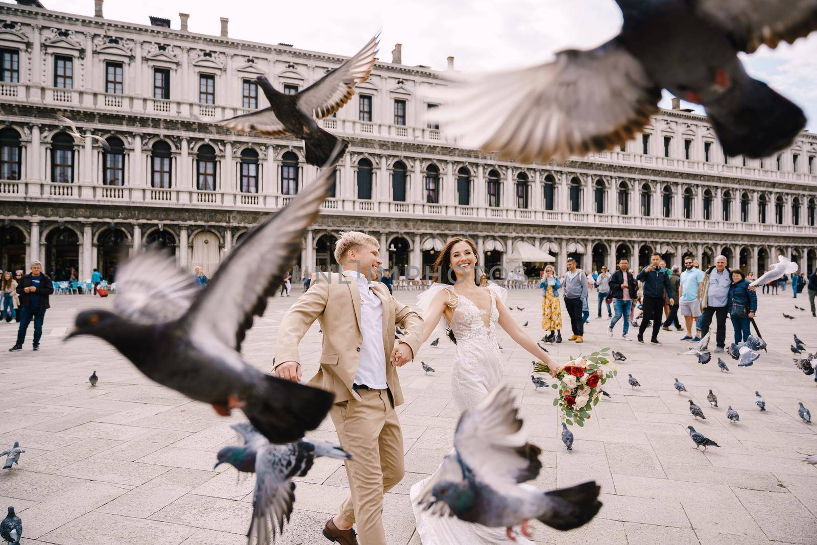 Venice, Italy - 04 october 2019: Venice Wedding, Italy. The bride and groom are running through a flock of flying pigeons in Piazza San Marco, amid the National Archaeological Museum Venice by Nadtochiy