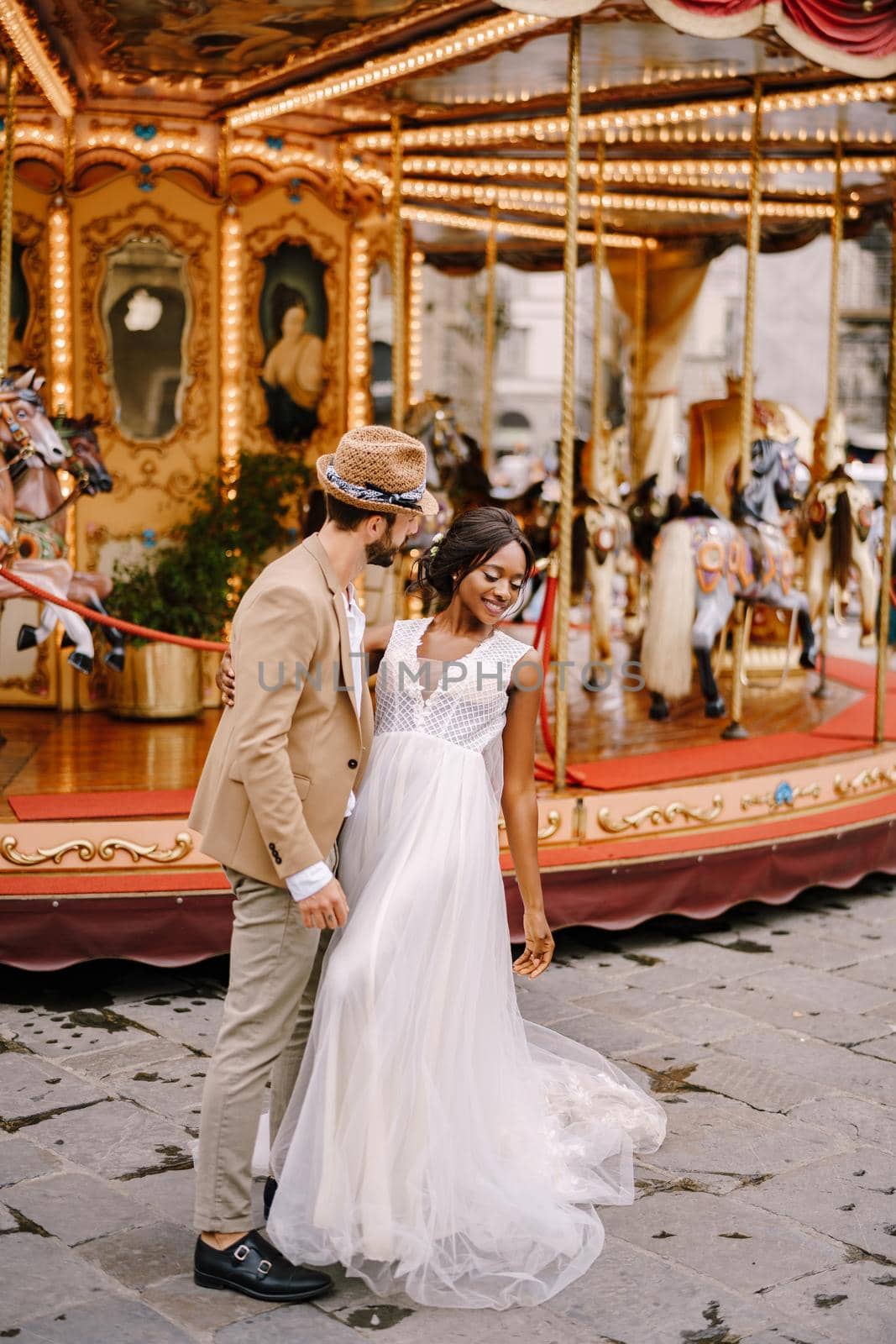 African-American bride and Caucasian groom near the carousel. Interracial wedding couple. Wedding in Florence, Italy