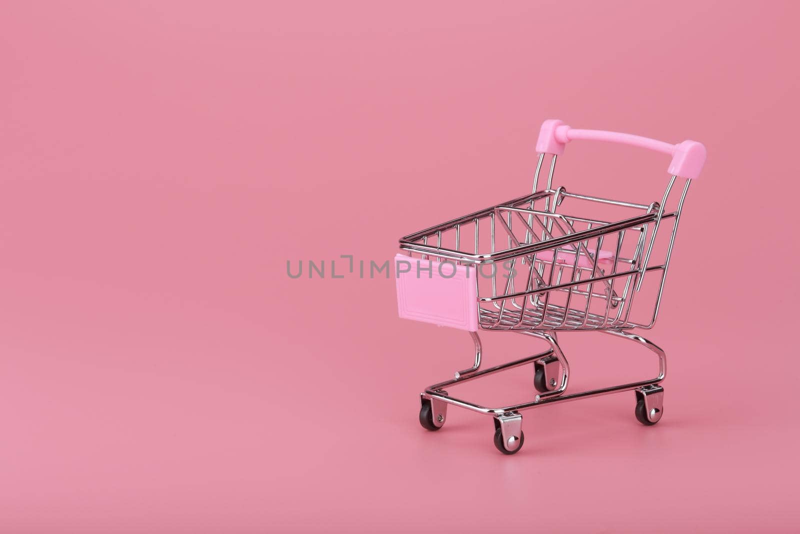 Shopping cart against pink background with copy space. Concept of online shopping and commerce by Senorina_Irina