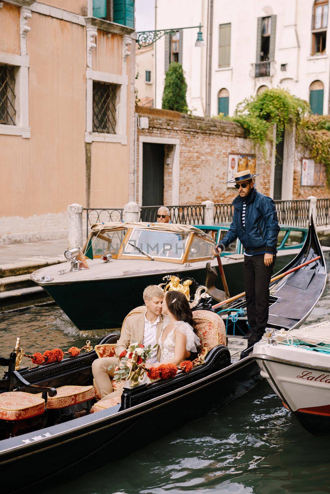 Venice, Italy - 04 october 2019: Italy wedding in Venice. A gondolier rolls a bride and groom in a classic wooden gondola along a narrow Venetian canal. Newlyweds are sitting in a boat by Nadtochiy