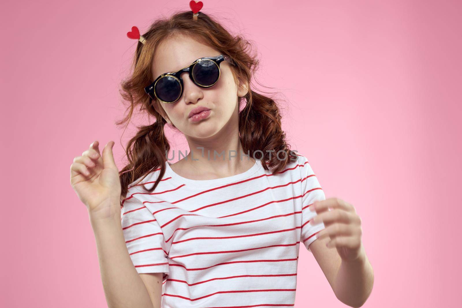 little girl in fashionable glasses and clothespins on her hair emotions pink background hearts. High quality photo