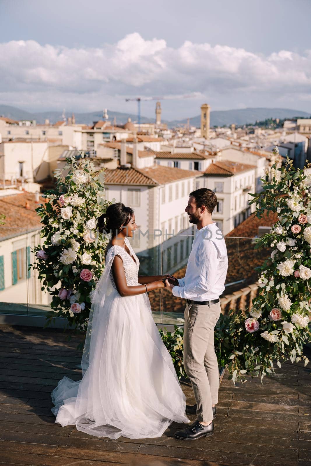 Interracial wedding couple. Destination fine-art wedding in Florence, Italy. A wedding ceremony on the roof of the building, with cityscape views of the city and Cathedral of Santa Maria Del Fiore