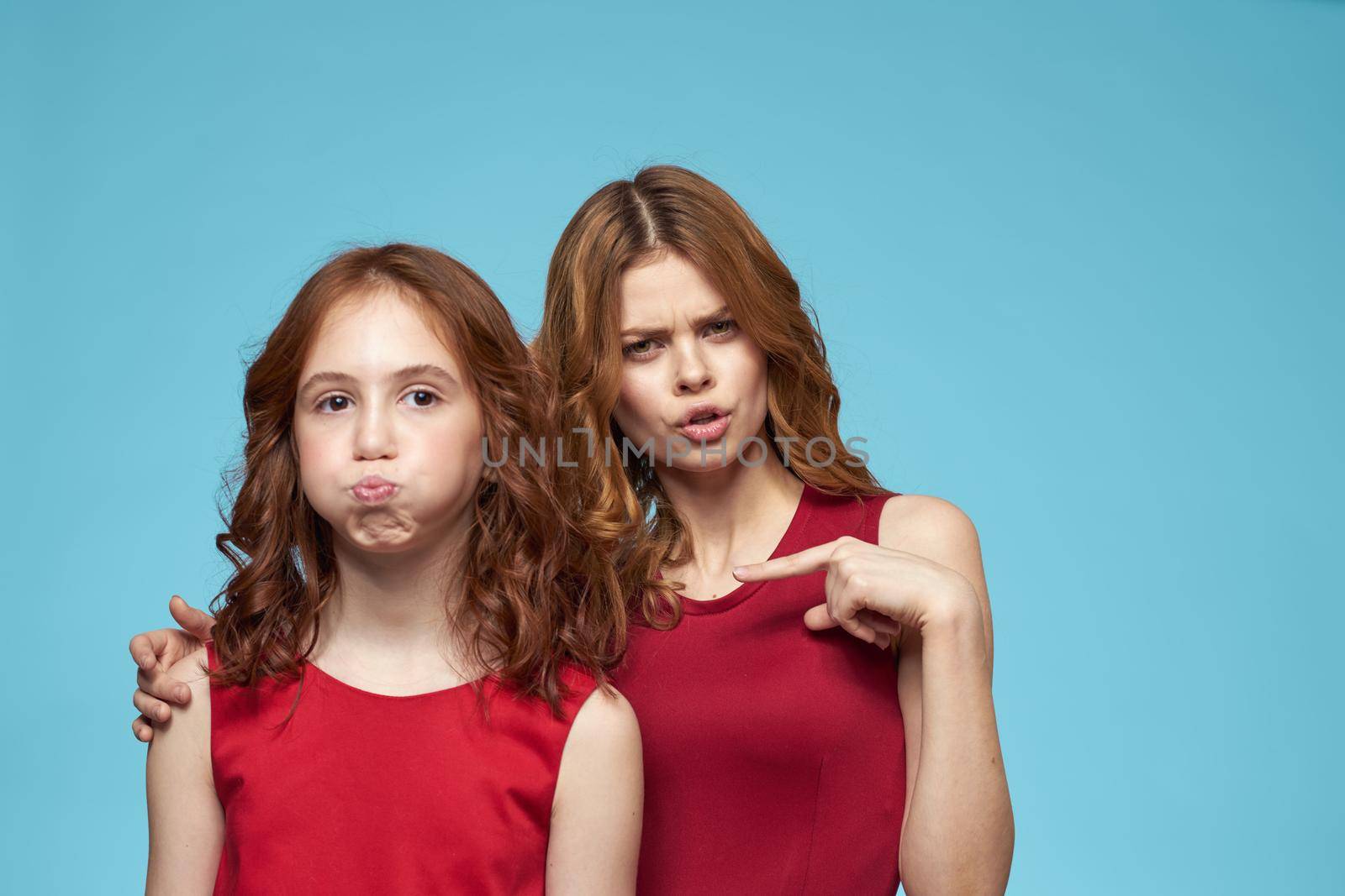 Mom and daughter in red dresses entertainment lifestyle fun studio blue background. High quality photo