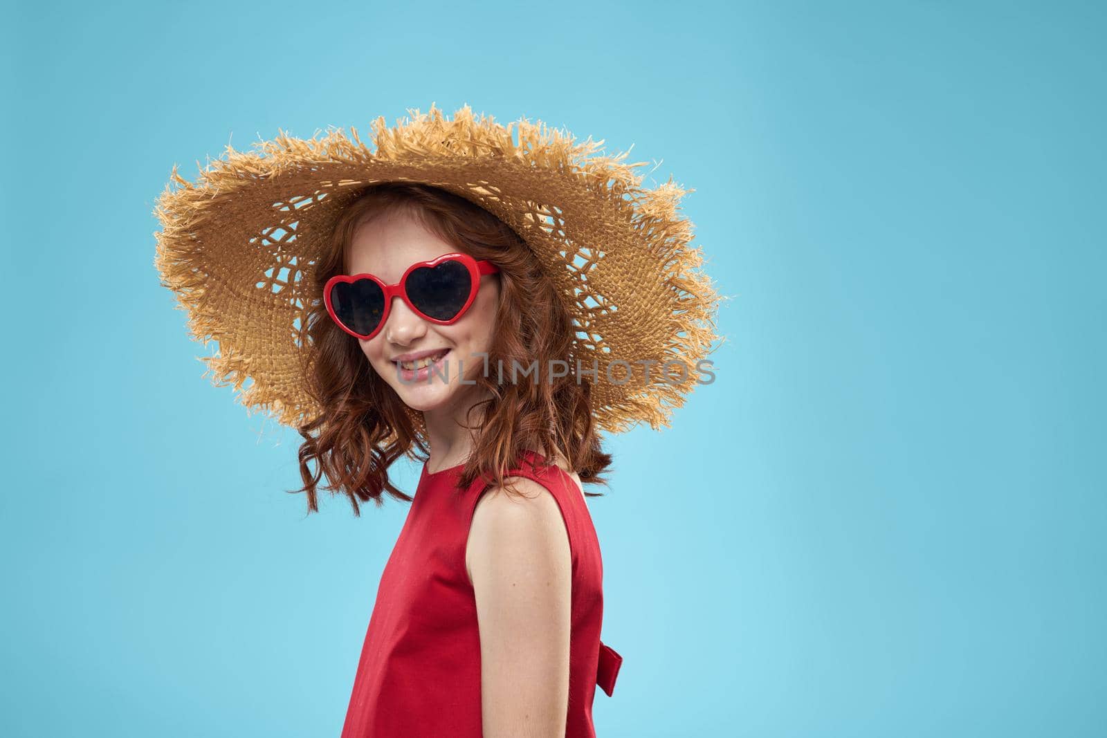 Girl in a beach Straw hat in sunglasses curly hair fun blue background. High quality photo