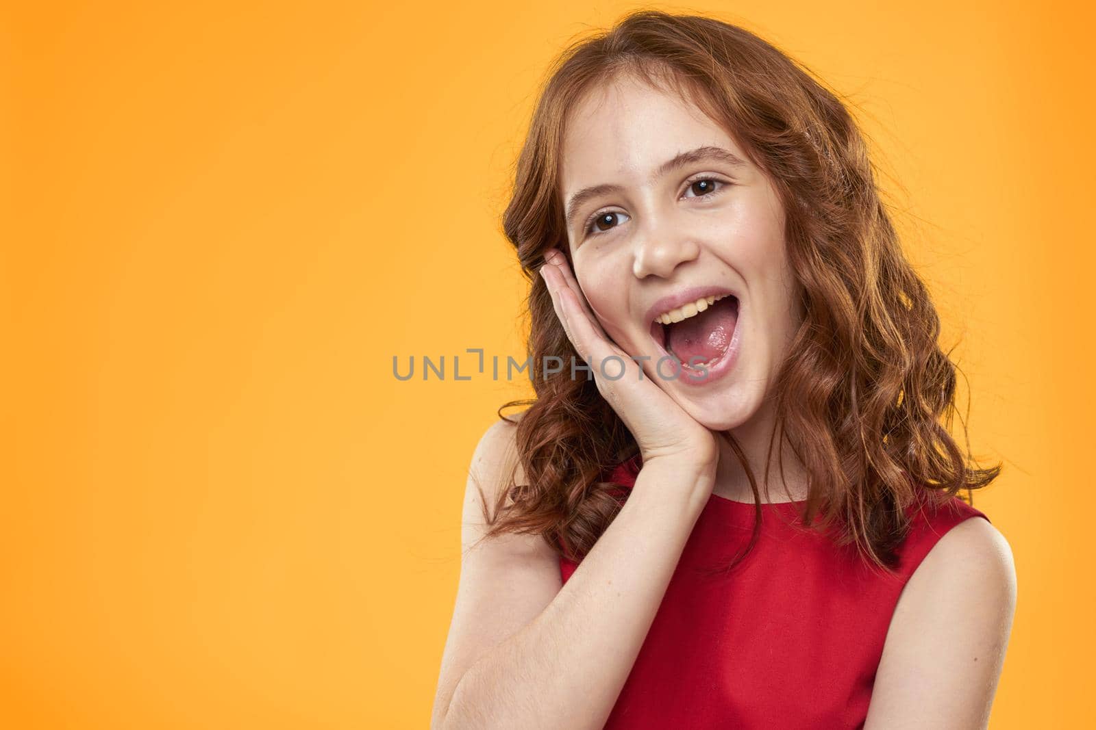 Girl with curly hair red dress fun childhood emotions yellow background. High quality photo