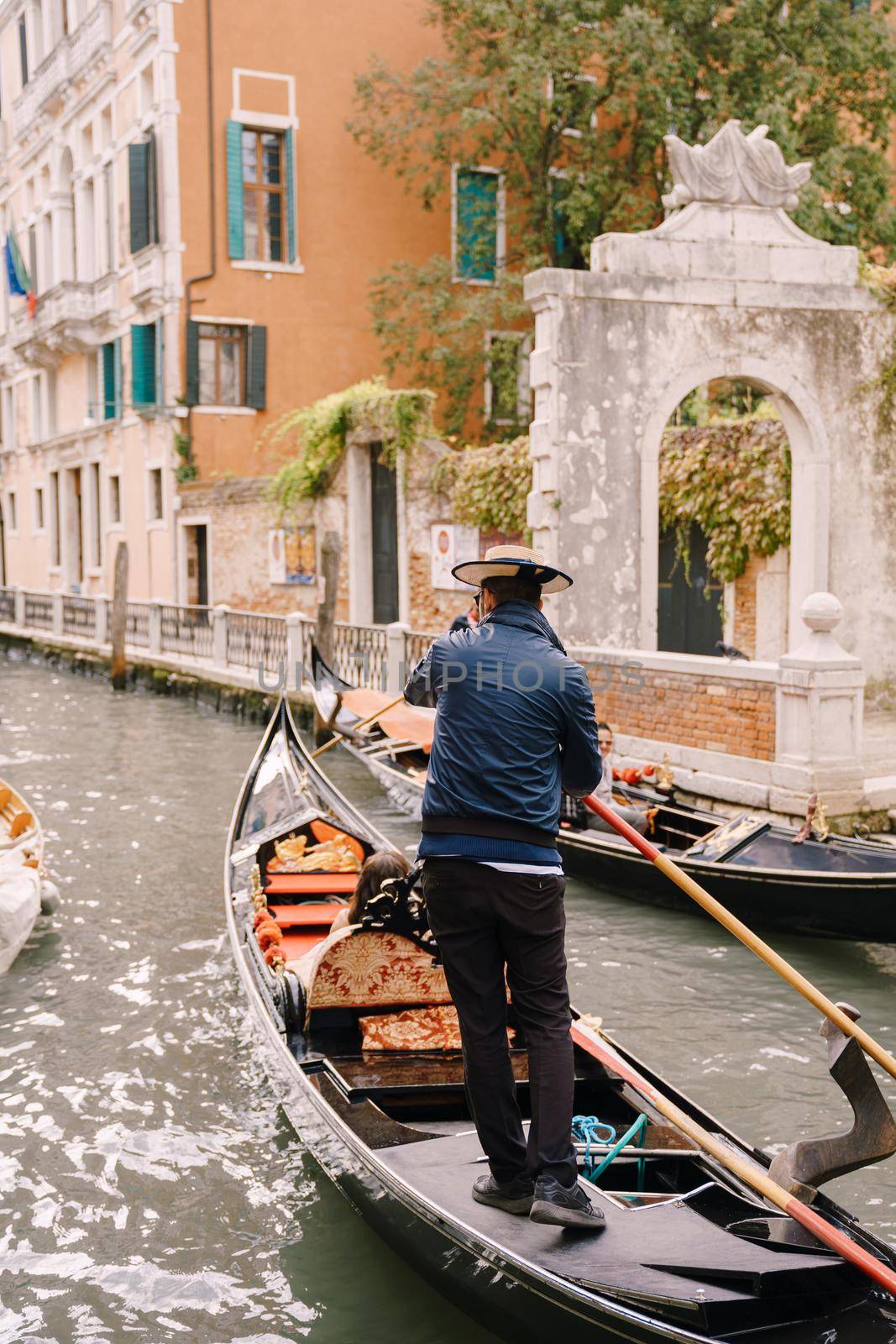 The gondolier rides the bride and groom in a classic wooden gondola along a narrow Venetian canal. The spin of the gondolier is controlled by a boat with a paddle.