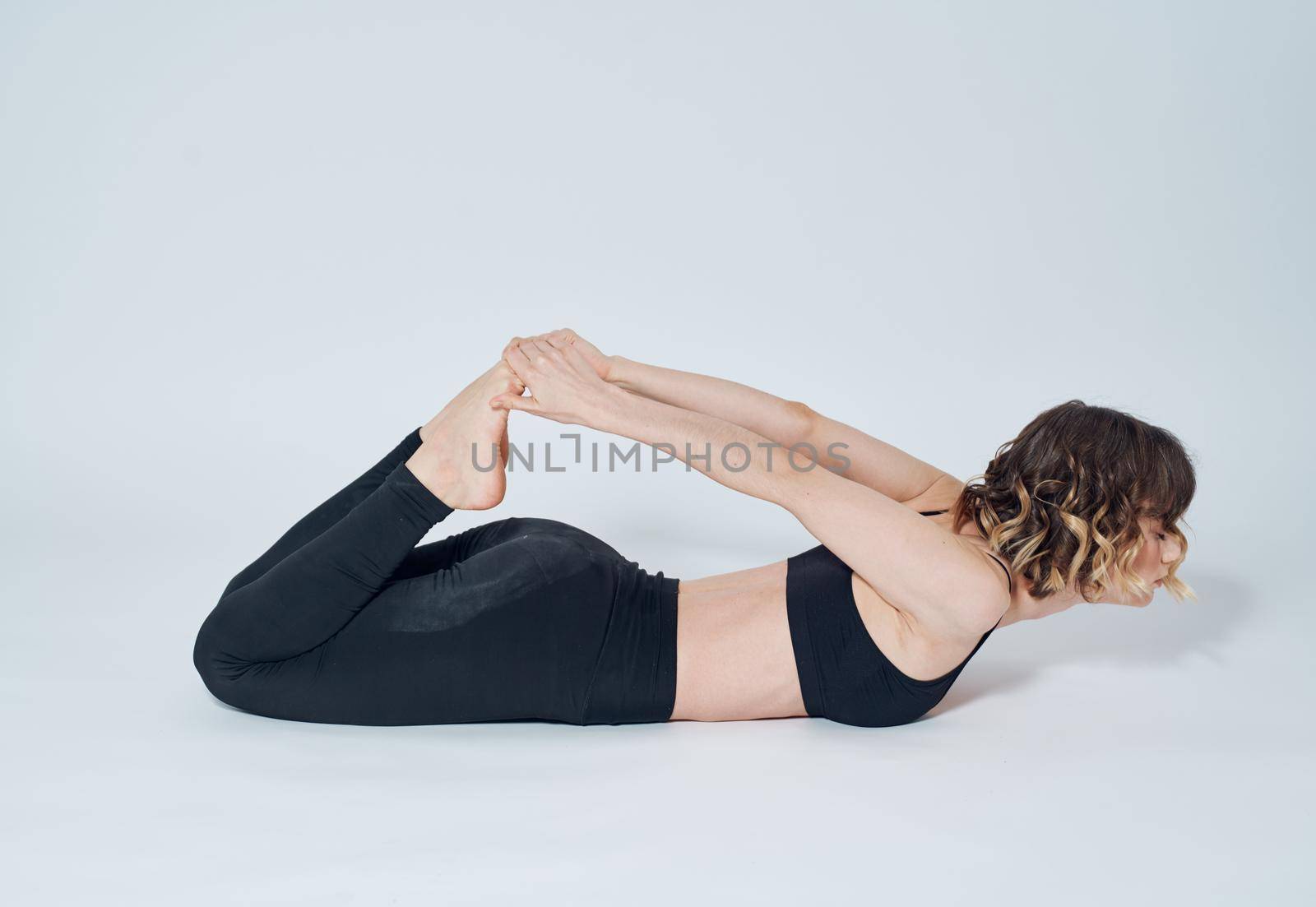 A woman lies on her stomach and touches her toes gymnastics yoga asana by SHOTPRIME