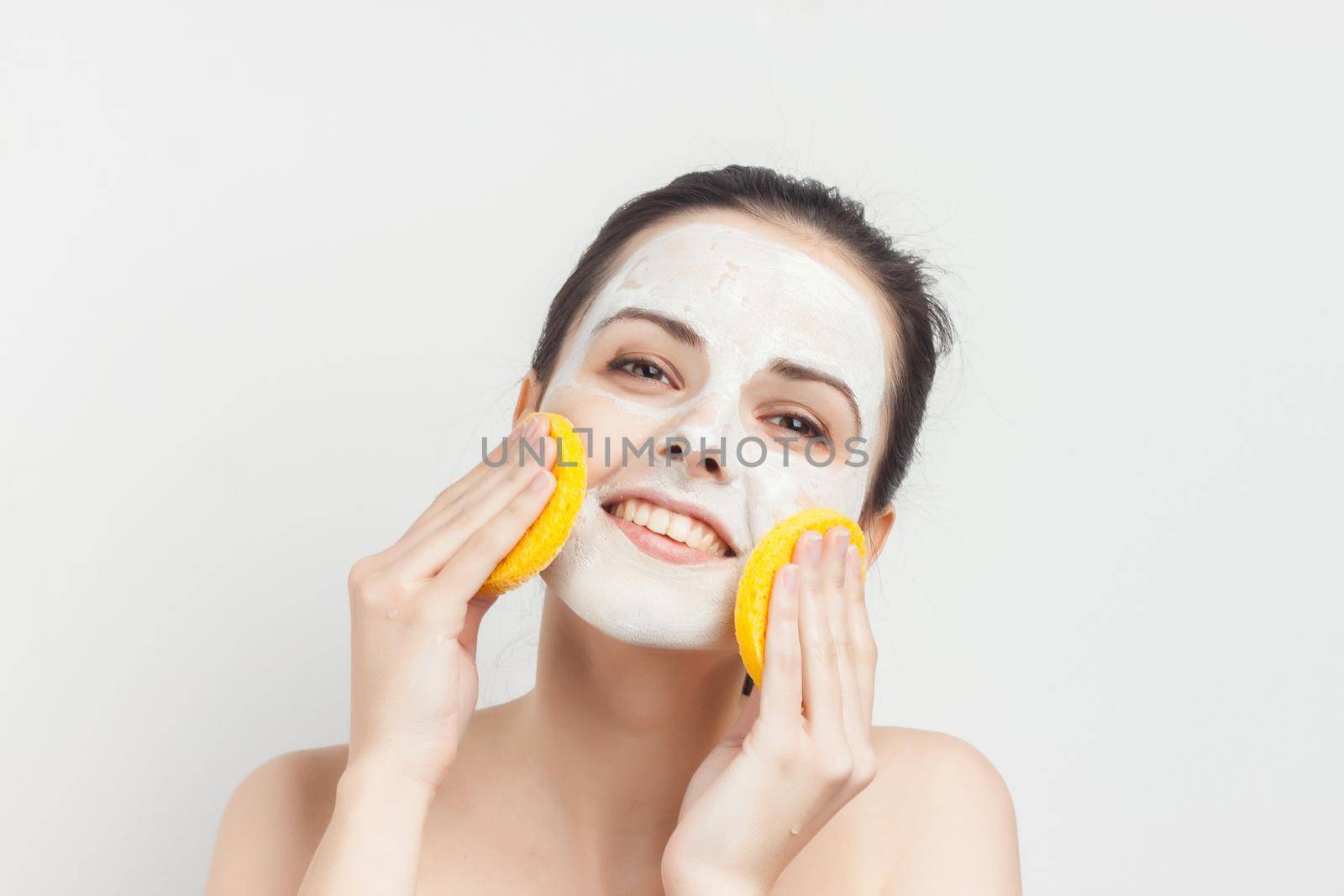 cheerful woman naked shoulders sponges in hands mask on face. High quality photo