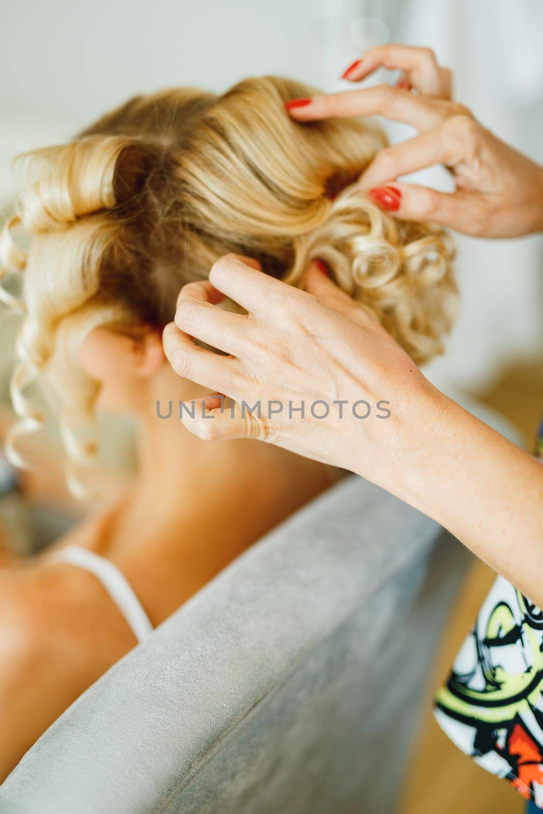 The stylist fixes the styling for a woman with long blond hair using hairspray . High quality photo