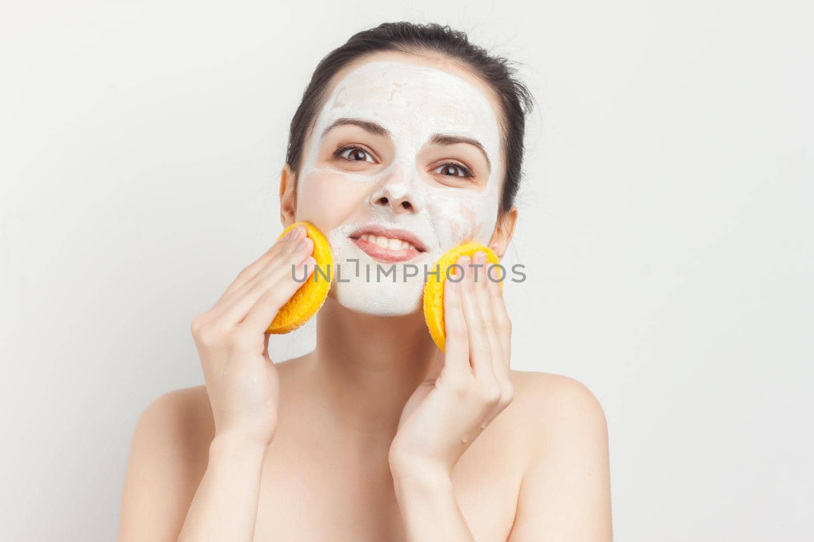 cheerful brunette with bare shoulders face mask sponges in hands skin care. High quality photo