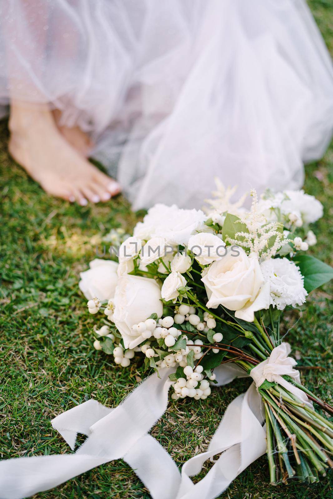 Wedding in Florence, Italy, in an old villa-winery. The white bouquet of the bride lies on the grass, barefoot legs of the bride.