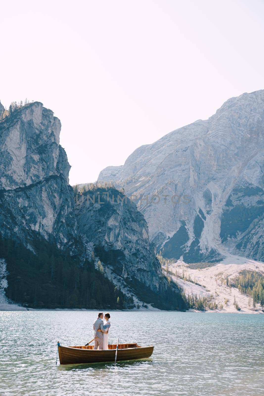 Bride and groom sailing in wooden boat, with oars at Lago di Braies lake in Italy. Wedding in Europe - Newlyweds are standing embracing in boat