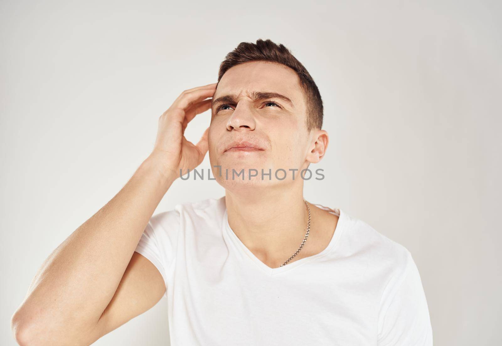 Pensive man in a white T-shirt touches his face with his hand on a light background portrait of a model. High quality photo
