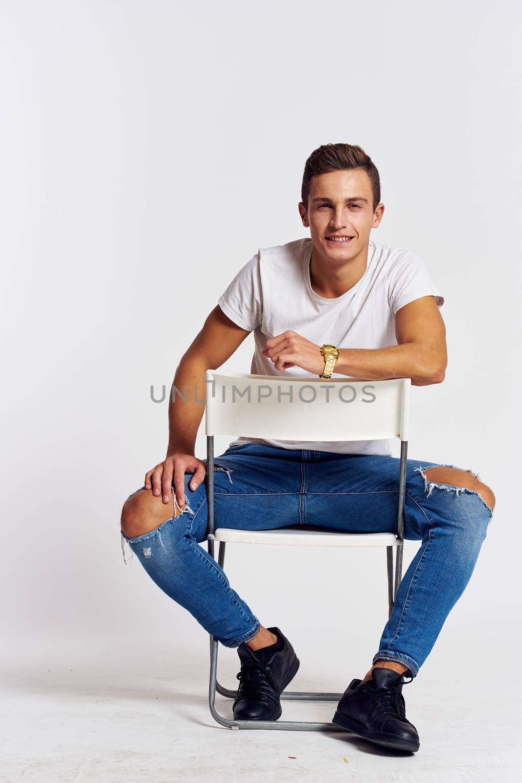 A man in jeans sits on a chair backwards and and ripped jeans T-shirt front view. High quality photo
