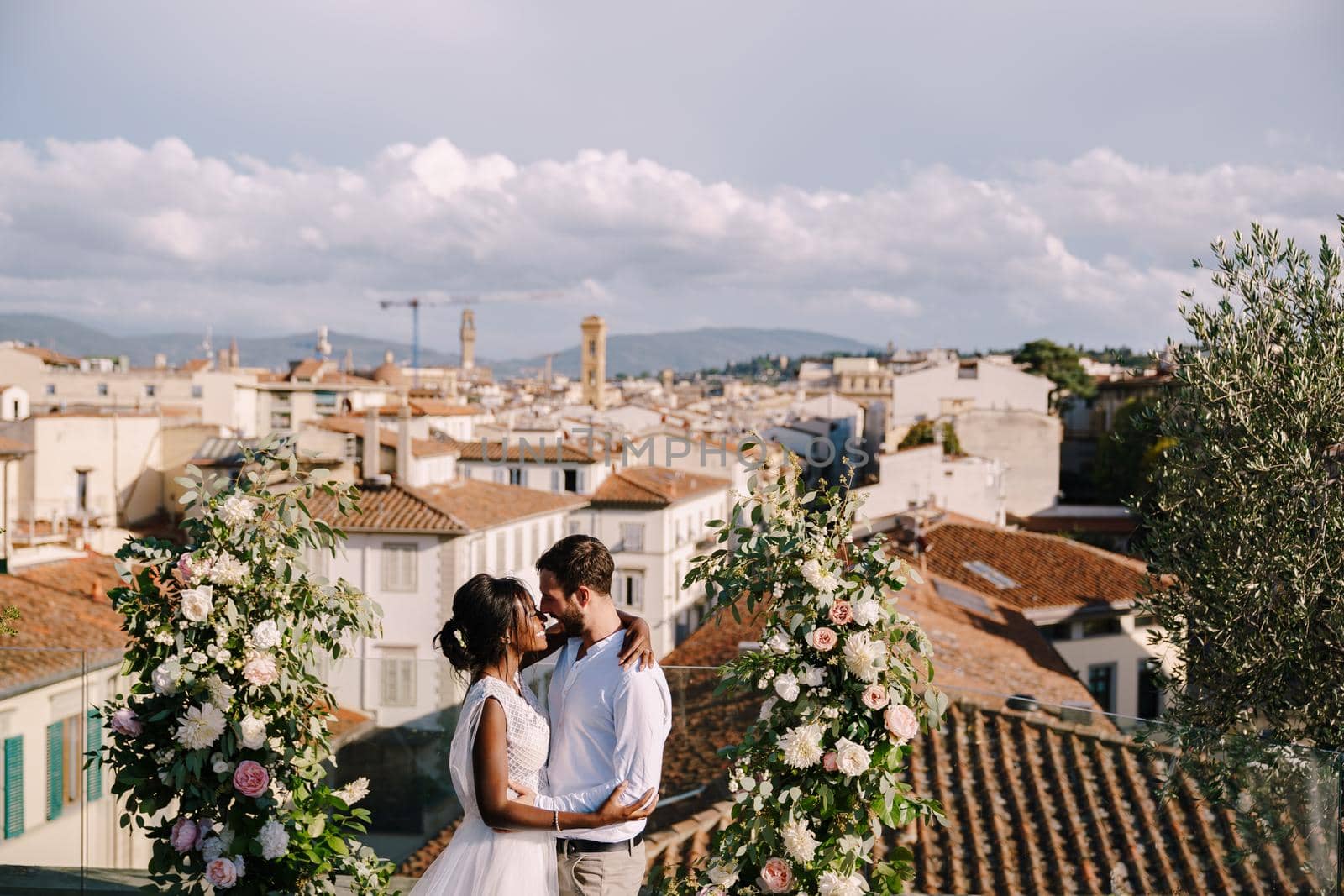 Interracial wedding couple. A wedding ceremony on the roof of the building, with cityscape views of the city and the Cathedral of Santa Maria Del Fiore. Destination fine-art wedding in Florence, Italy by Nadtochiy