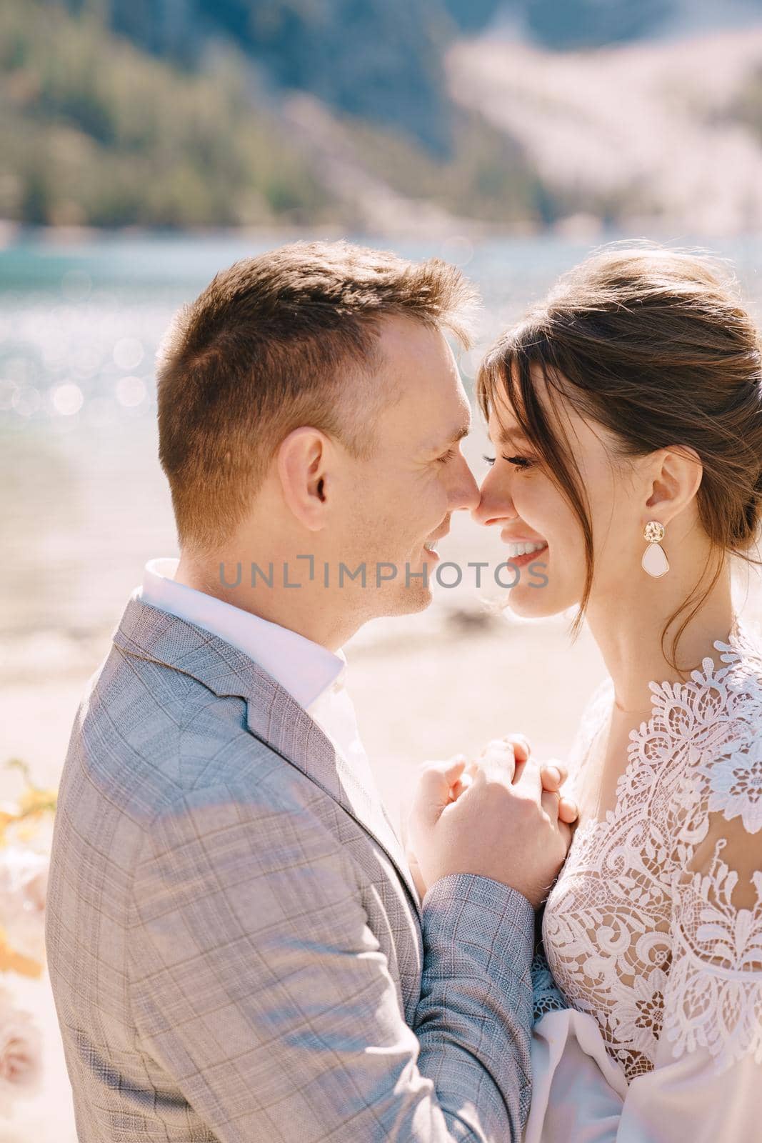 Newlyweds kiss on the spot for the ceremony, with an arch of autumn flower columns, against the backdrop of Lago di Braies in Italy. Destination wedding in Europe, at Braies lake.