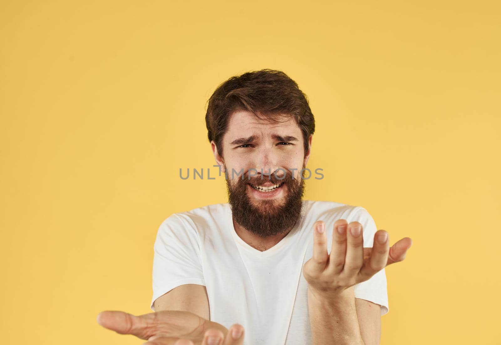 Emotional guy in a white t-shirt on a yellow background gesturing with his hands cropped view. High quality photo