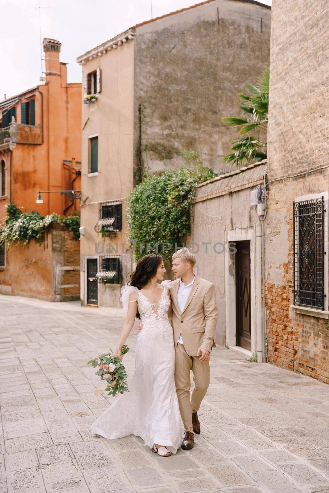 Italy wedding in Venice. The bride and groom walk along the deserted streets of the city. The newlyweds hug, dance, hold hands against the backdrop of picturesque red brick houses. by Nadtochiy