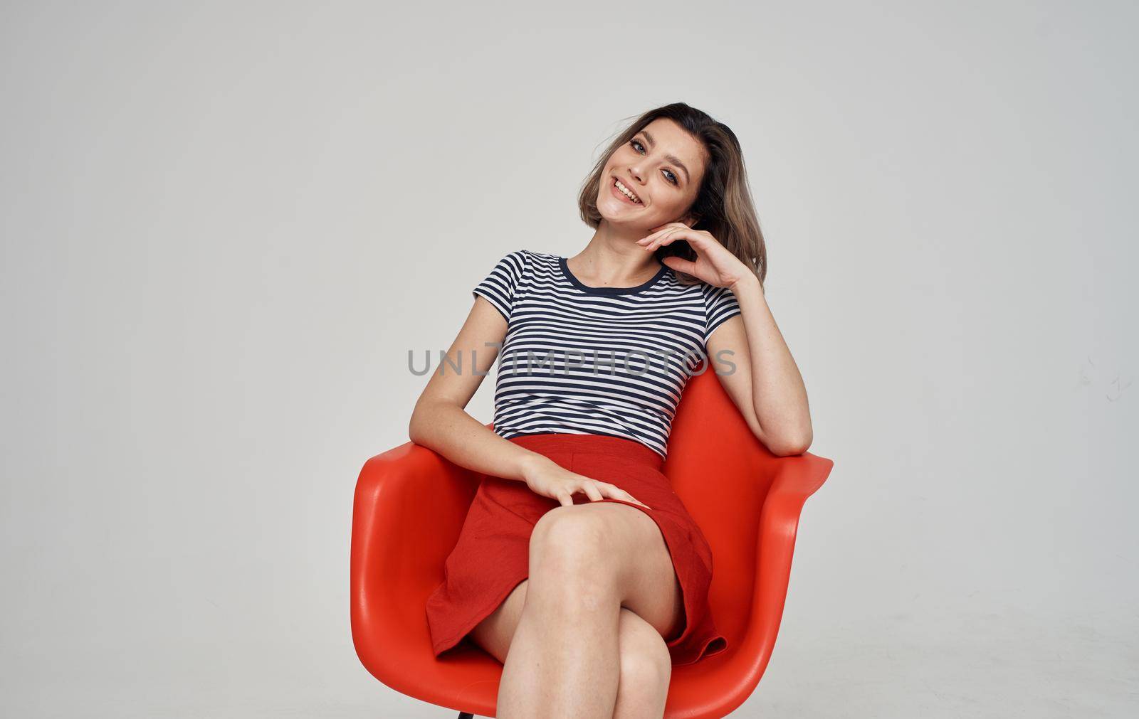 a woman in a skirt and a striped T-shirt sits on a red chair In a bright room. High quality photo