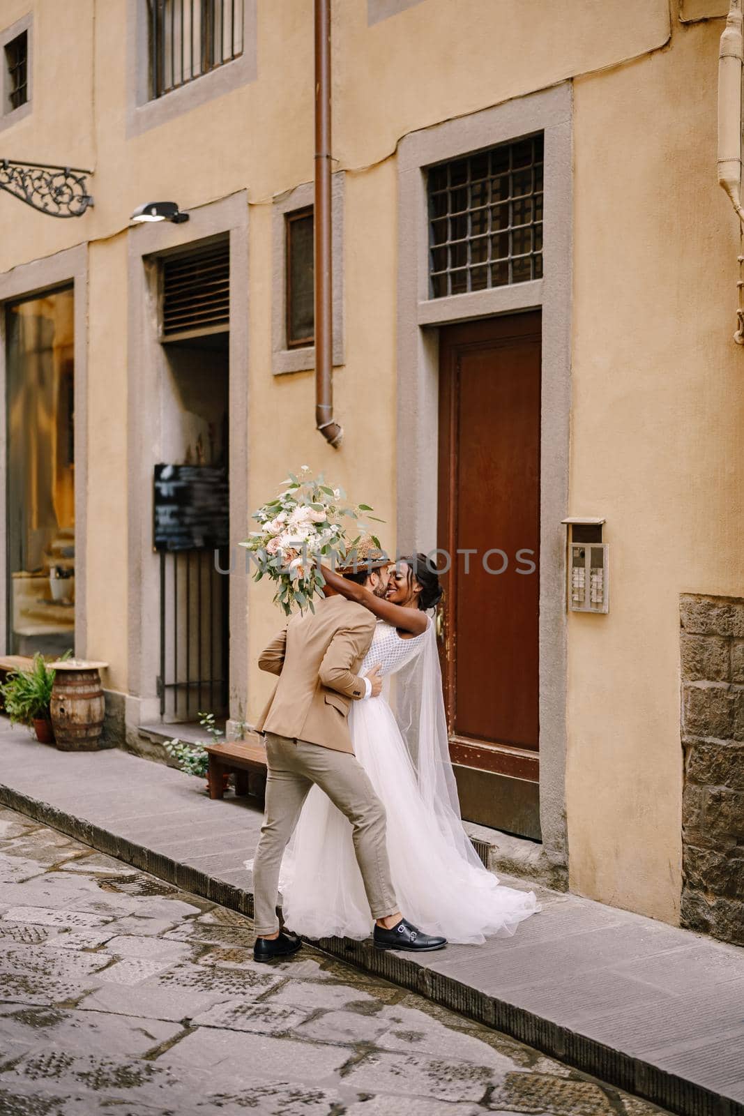 Interracial wedding couple. Wedding in Florence, Italy. African-American bride and Caucasian groom kiss on the street. by Nadtochiy