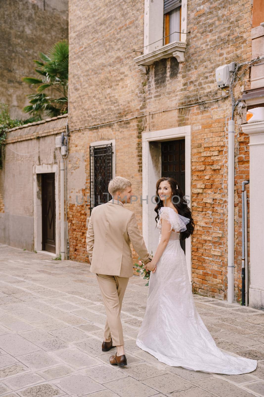 The bride and groom walk through the deserted streets of the city. Newlyweds hug, dance, hold hands against the backdrop of picturesque red brick houses.