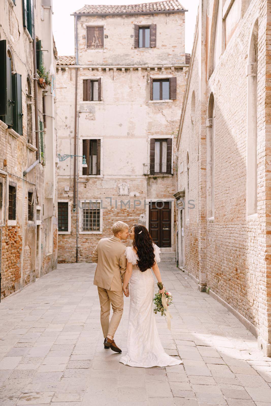 The bride and groom walk through the deserted streets of the city. Newlyweds walk in a dead-end alley against the background of brick buildings.