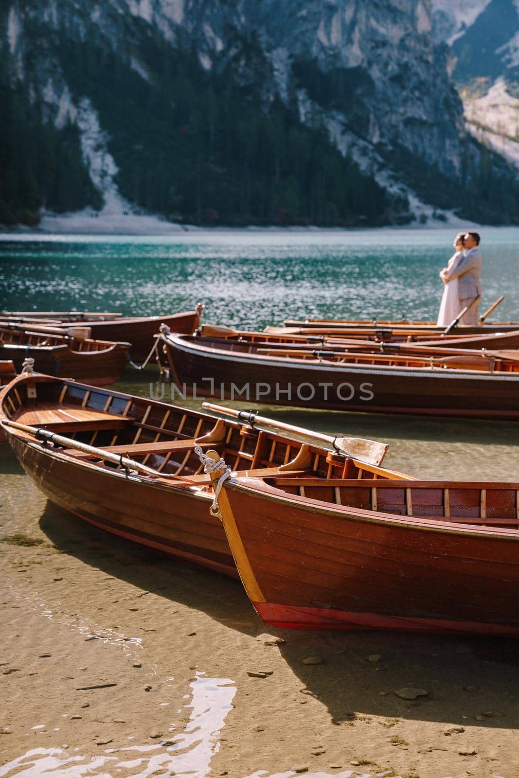 Bride and groom sailing in wooden boat, with oars at Lago di Braies lake in Italy. Wedding in Europe - Newlyweds are standing embracing in boat