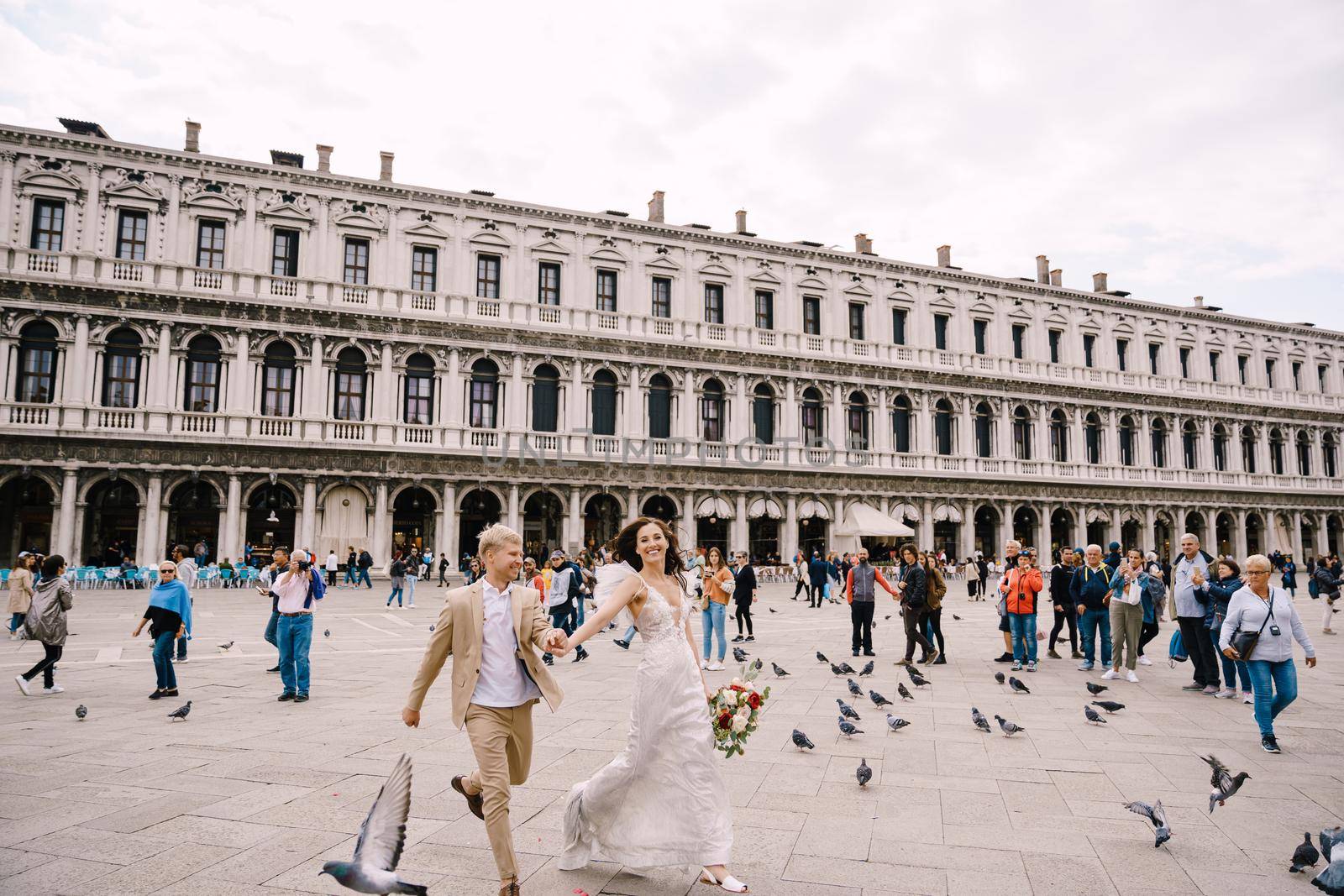 Venice, Italy - 04 october 2019: Venice Wedding, Italy. The bride and groom are running through a flock of flying pigeons in Piazza San Marco, amid the National Archaeological Museum Venice by Nadtochiy