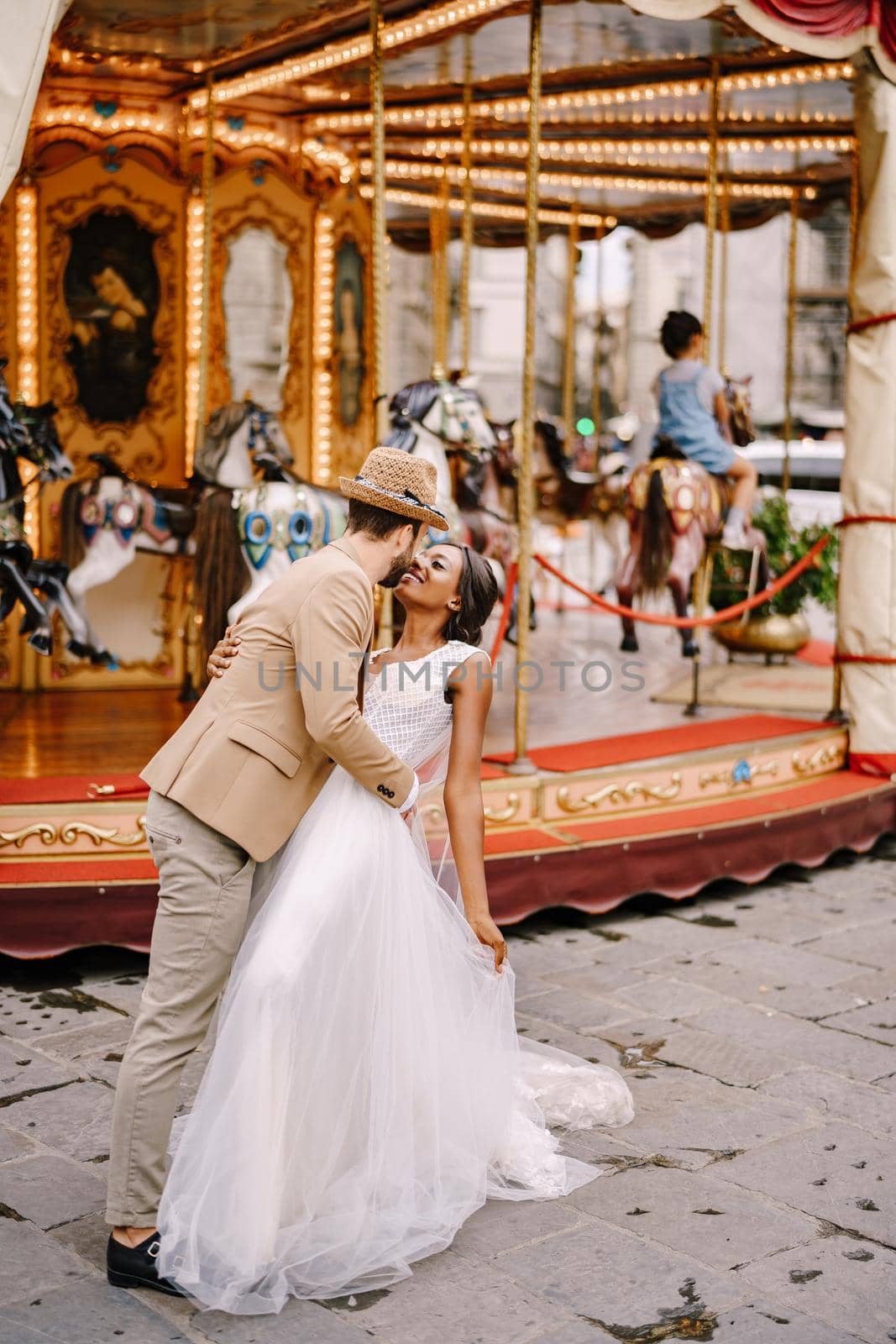 African-American bride and Caucasian groom near the carousel. Interracial wedding couple. Wedding in Florence, Italy