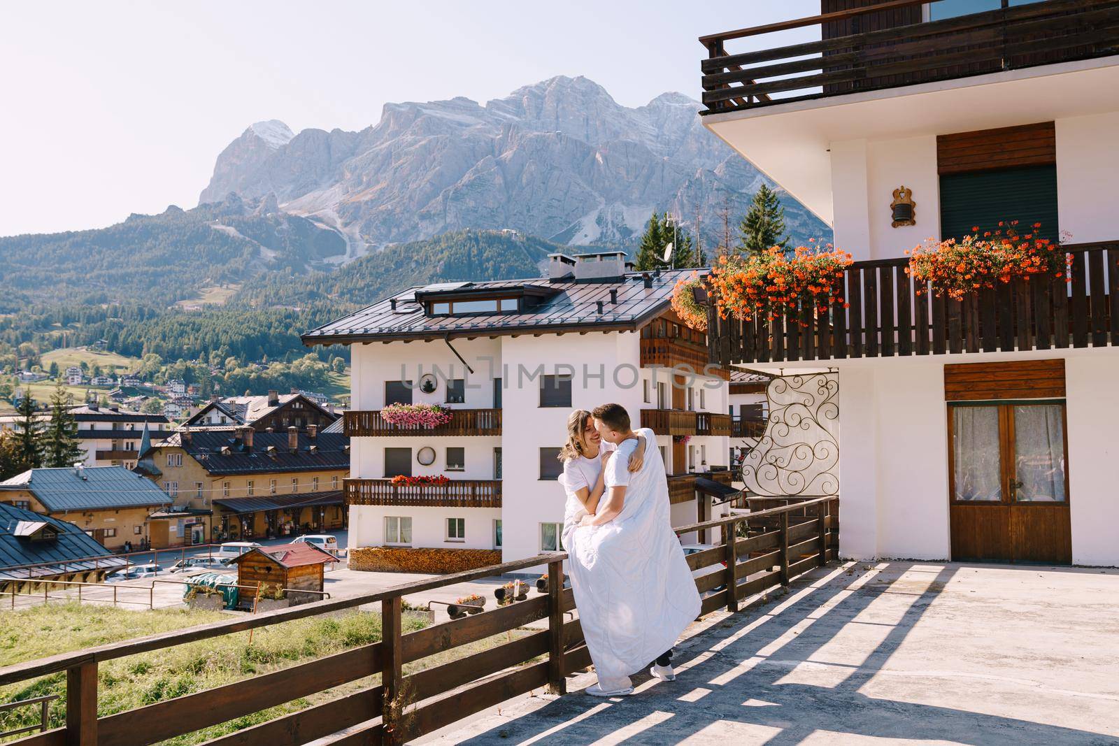 A guy and a girl cuddle with a blanket outside a hotel in the mountains. Cortina Ampezzo is an Italian city in province of Belluno in Veneto region, a winter resort in Dolomites by Nadtochiy