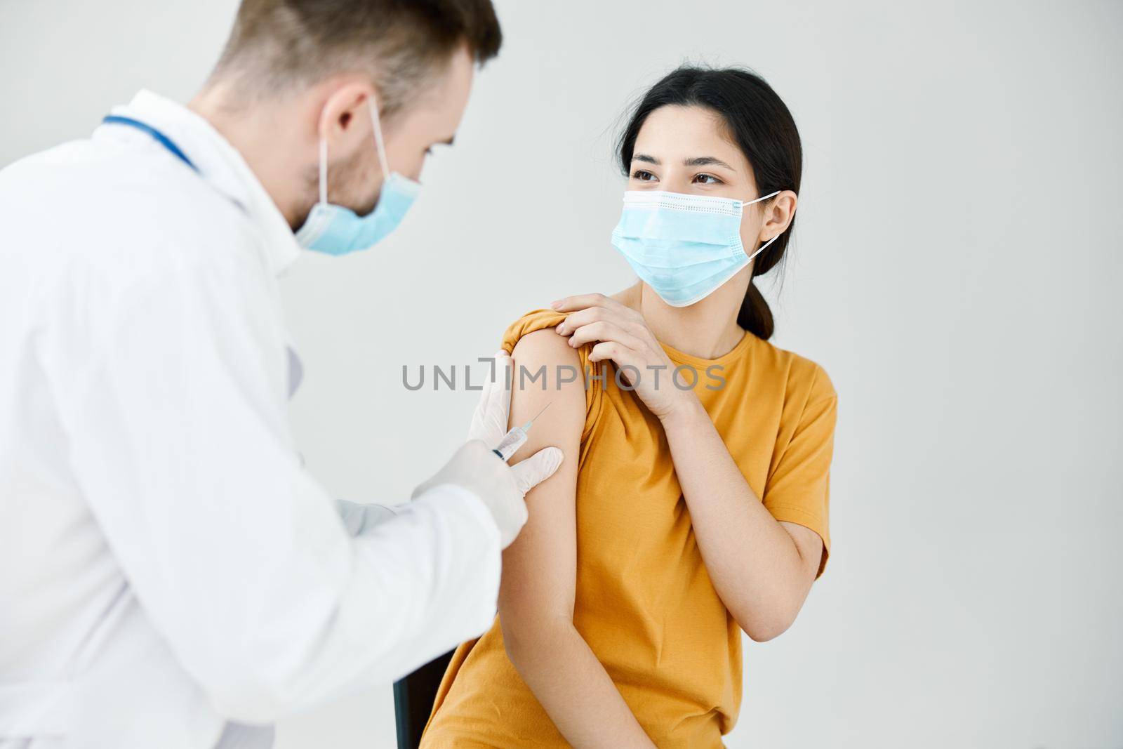 doctor injecting a woman in a yellow t-shirt in the shoulder close-up covid vaccination by SHOTPRIME