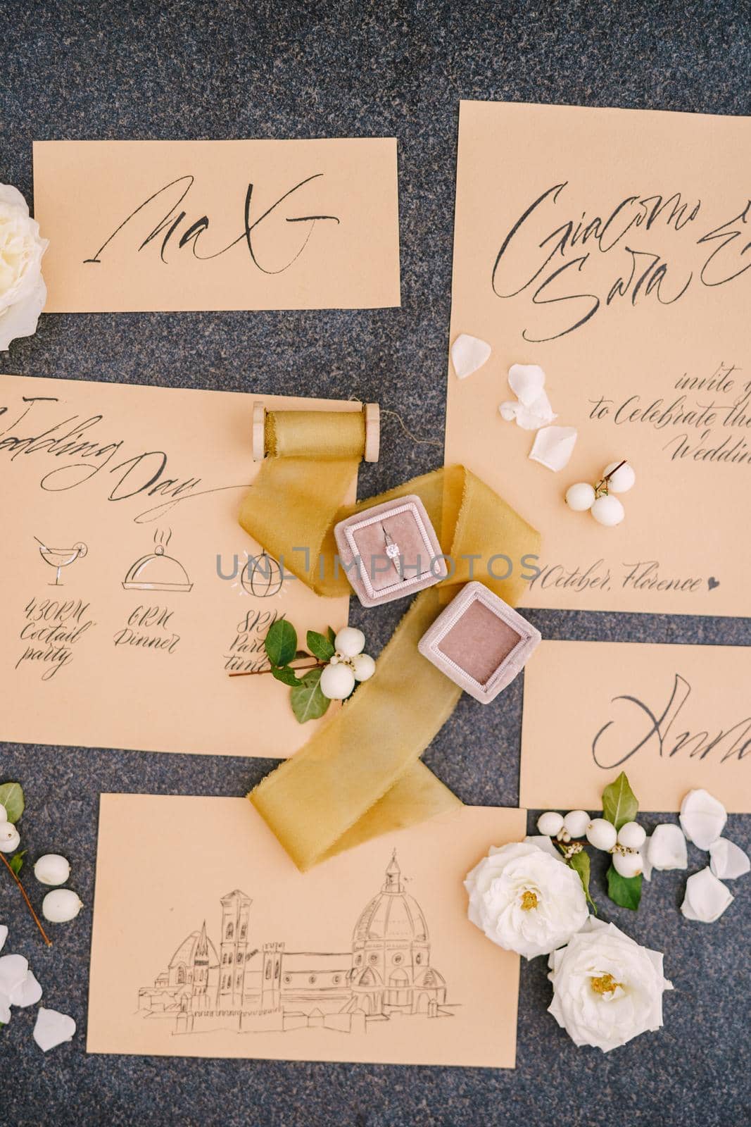 Wedding rings in a box, invitation cards, silk ribbon, white roses on black background. Overhead top view