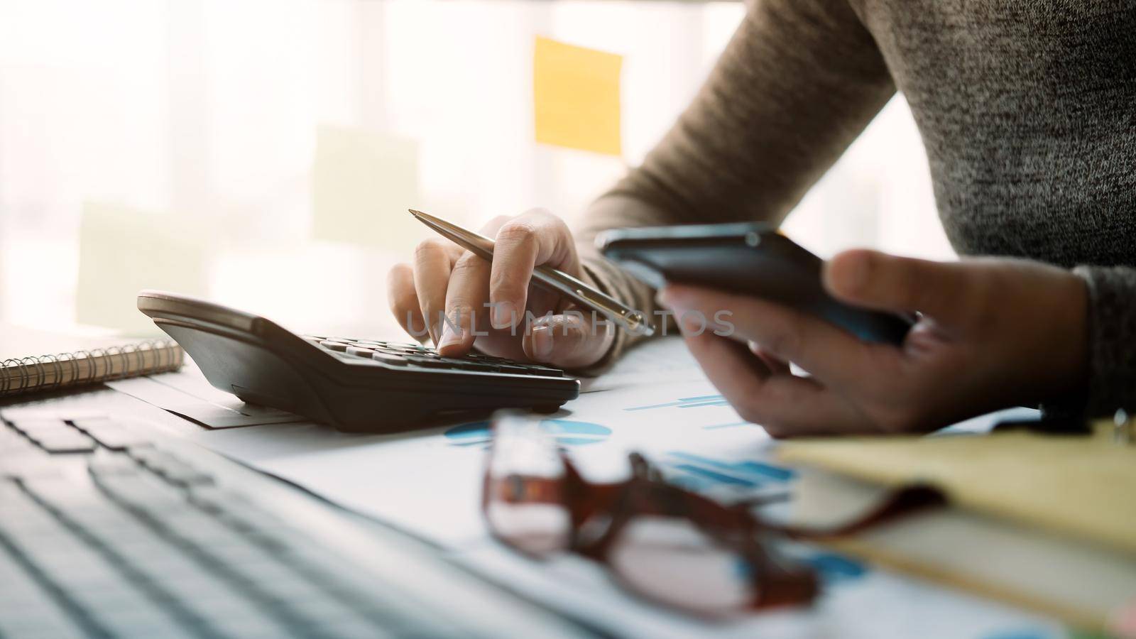 Business woman working with calculator and smartphone for analyzing company financial report balance  by nateemee