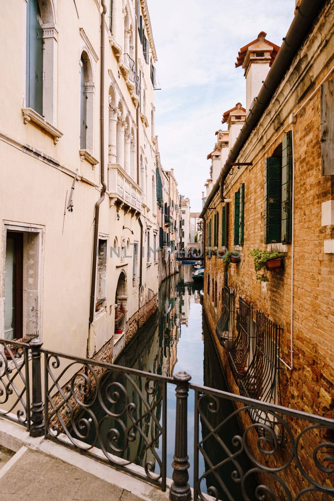 Beautiful narrow canal in Venice, Italy. Small stone bridge connects houses from both sides of the canal. Building facades are aged by weather and water.