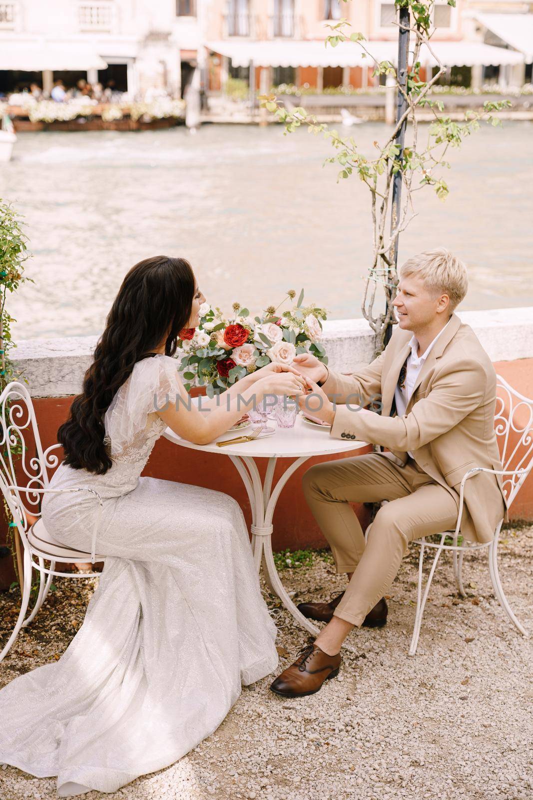 The bride and groom sit at tables on the banks of the Grand Canal and hold hands in Venice, Italy. The most romantic place on earth. Waiting for a romantic dinner for two.