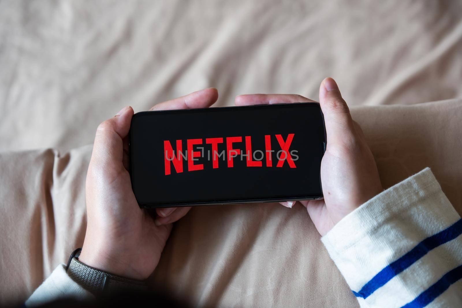 CHIANG MAI,THAILAND - APR 06, 2020 : Woman using iPhone X open Netflix application at home. Netflix is a global provider of streaming movies and TV series.