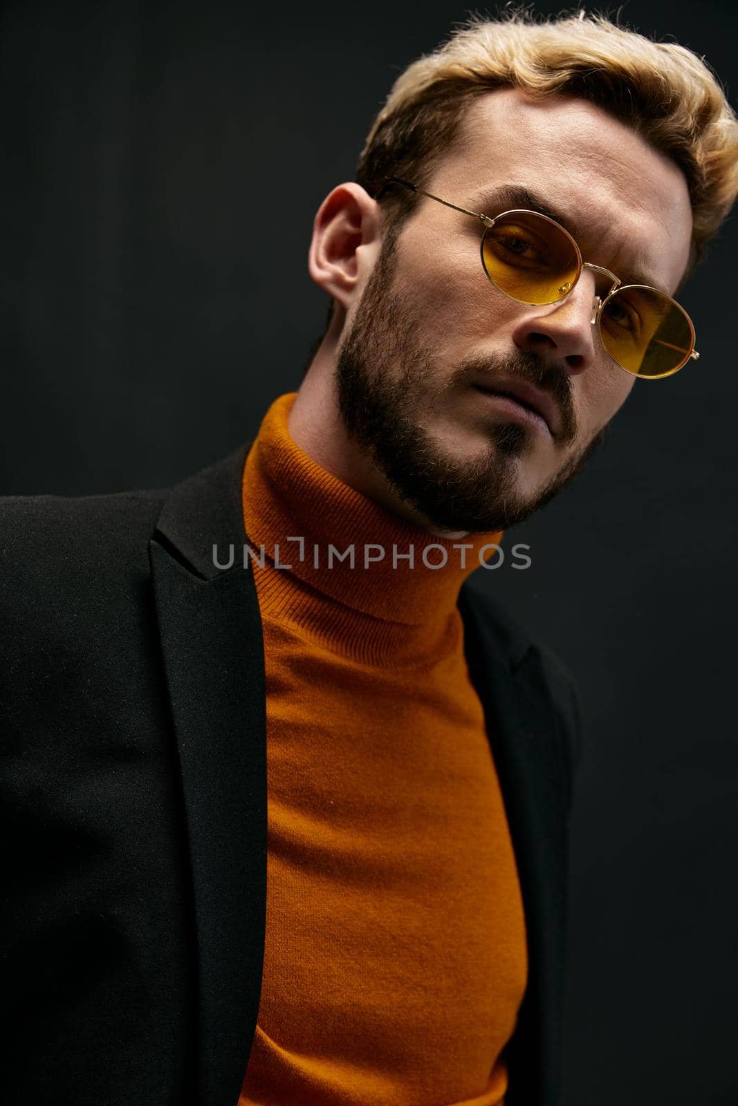 stylish man in yellow glasses and an orange sweater bent over to the side against a dark background. High quality photo